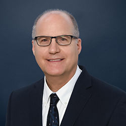 David Everson smiles into the camera against a dark blue background.